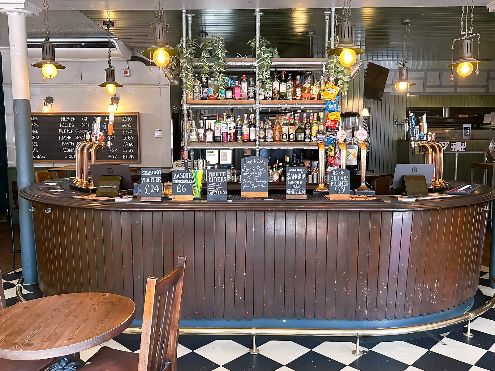 Head-on view of the horseshoe bar: copper taps, the chalkboard tap list, hanging lamps and specials boards along the counter