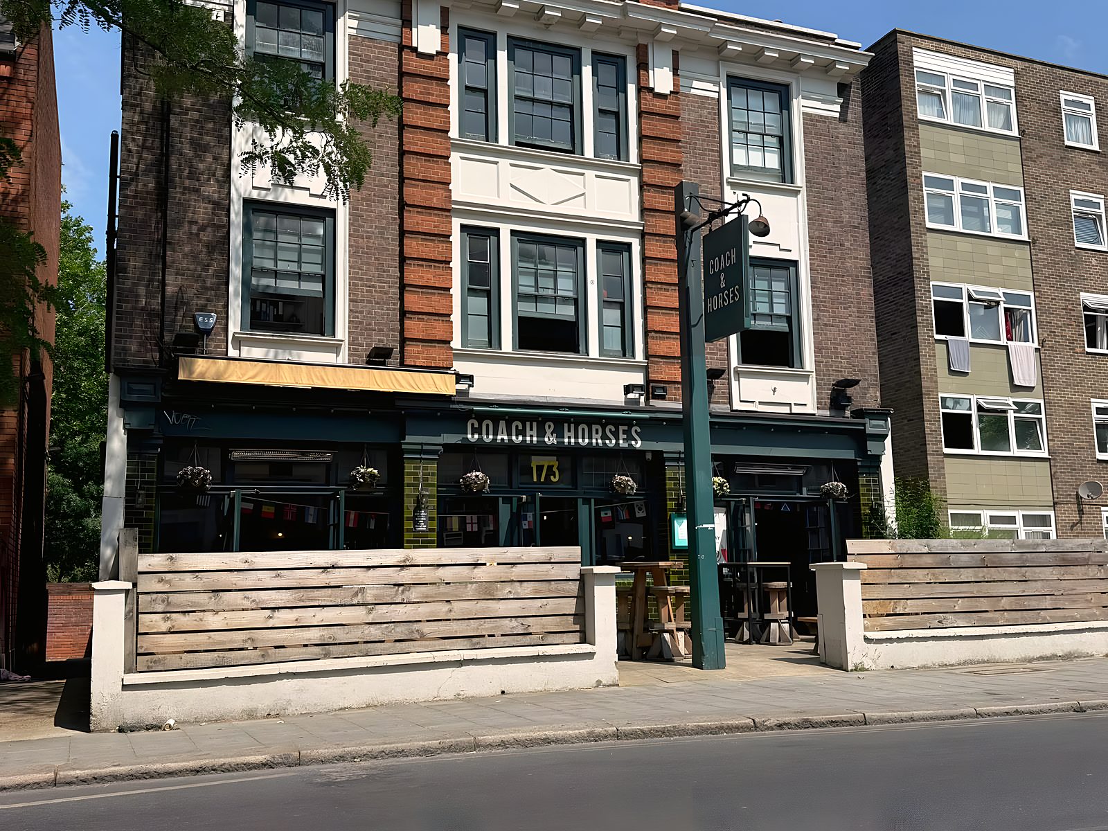 Close view of the frontage with hanging baskets, terrace benches and the hanging pub sign